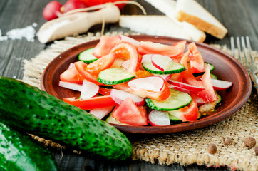 
healthy salad with fresh ripe summer vegetables , tomato, cucumber , radishes , spices and white toast on a wooden background