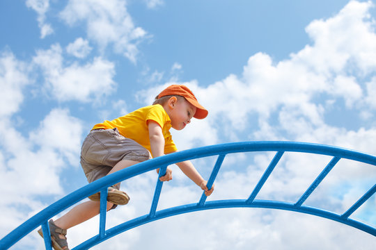 little boy climbs up the ladder on the playground. child climbs confidently up the ladder against the blue sky. copy space for your text
