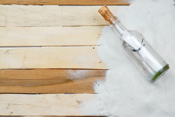 Summertime image with beachy theme of clean white sand scattered on boardwalk planks with a message in a bottle making a right side border with copy space