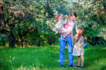 Fototapeta premium Adorable little girls with young father in blooming cherry garden 