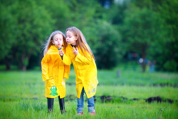 Funny cute toddler girls wearing waterproof coat playing outdoors by rainy and sunny day