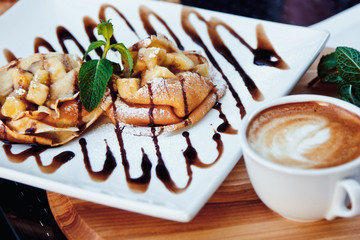 pancakes with chocolate and fruit and coffee on wooden background. Beautiful restaurant serving the dessert