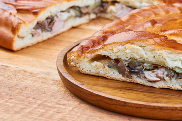 Slice of pie with chicken and mushrooms on wooden plate