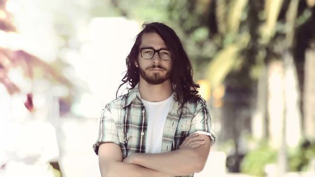 Young man portrait in a park. Middle twenties. Long hair, blue  eyes and glasses. Instagram filter style.