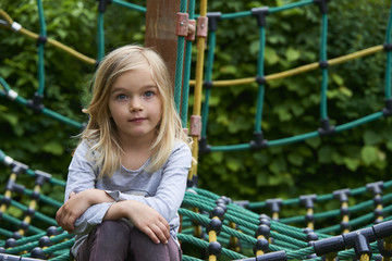 Portrait of Happy little blond girl playing on a rope web playground outdoor