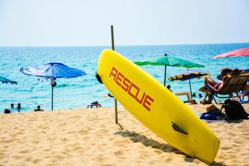 A rescue surf board standing on a beach in Phuket, Thailand with lots of tourists.