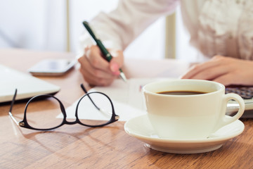 Businesswoman writing and drink coffee at desk
