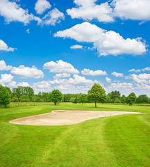 Green golf course field and blue cloudy sky