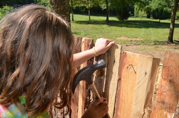 Young girl building a fort - playhouse in the summertime sunshine.  Youthful childhood outdoor activity.  Creating with wood, hammer and nails.