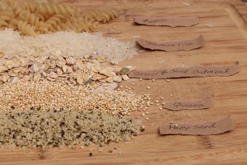 Foto op Canvas Multiple organic grains, including fusilli pasta, jasmine rice, quinoa, hemp seed, and a mix of grains and seeds oatmeal, on a cutting board on a rustic farm picnic table in summer. © SailingAway