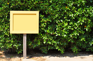 Blank yellow wooden sign on green leaves tree background