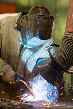 Industrial welder worker welding steel at factory workshop with flying sparks