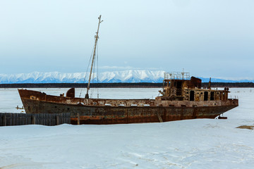 Old rusty ship on winter shore of Lake Baikal.