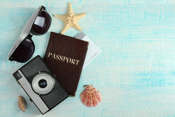 passport and ticket with a camera and sunglasses on a blue wooden background with different shapes of seashells