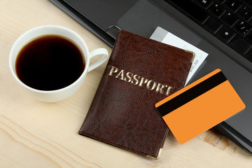 the passport with ticket and credit card on laptop keyboard on a brown wooden background with Cup of coffee.Set of trip stuff