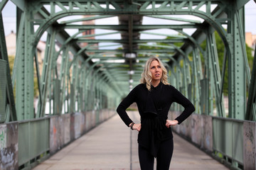 Beautiful blonde girl with black leggings and top standing on a bridge