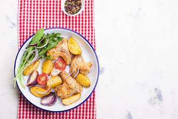 Homemade tasty roasted chicken wings with roasted potato with vegetables in an enamel bowl, top view, horizontal with place for text.