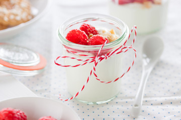 Homemade yogurt dessert with raspberries and crushed cookies in a small jar on a kitchen background, closeup