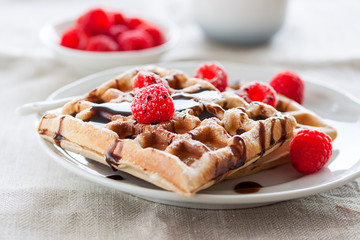 Tasty homemade waffles with raspberries and chocolate sauce ready for breakfast, closeup