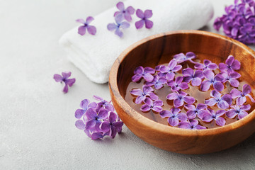 Obraz na płótnie Canvas Spa and wellness composition with perfumed lilac flowers water in wooden bowl and terry towel on gray stone background, aromatherapy