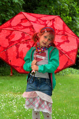 Mädchen steht mit rotem Regenschirm im Park