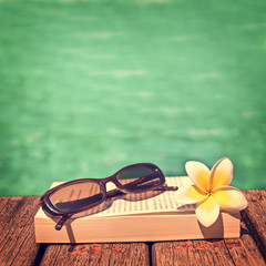 Fototapeta na wymiar Book and sunglasses, blue water background, vintage process