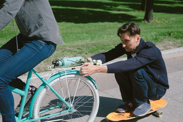 Young woman on bicycle pulling a man on a skateboard