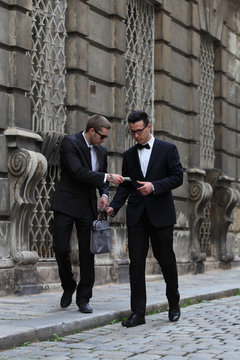 Two young men in black suits suspisciously exchange money and a computer bag on the street