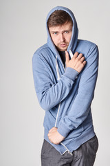 Handsome young man with light beard in blue hoodie,  on gray background