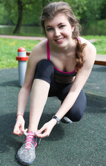 Pretty sportswoman tie shoelaces on a bench outdoors in park