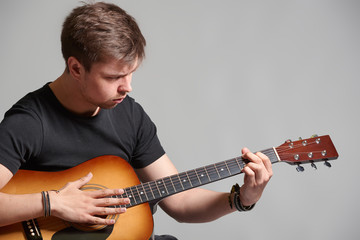 Young man with light beard playing acoustic guitar, on grey background