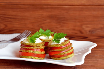Fried zucchini with fresh tomatoes, yogurt and parsley. Fried zucchini appetizer recipe. Easy vegetable snack. Roasted yellow squash in olive oil.  White napkin, fork, wooden table. Closeup