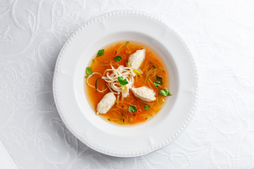 Chicken soup with noodles and vegetables in white bowl