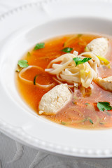 Chicken soup with noodles and vegetables in white bowl