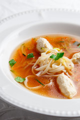 Chicken soup with noodles and vegetables in white bowl