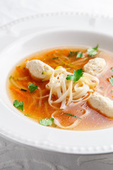 Chicken soup with noodles and vegetables in white bowl