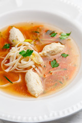 Chicken soup with noodles and vegetables in white bowl