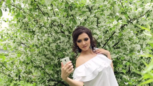 Happy woman taking selfie on smartphone in the blooming garden HD