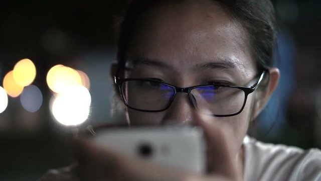 Black and white glassed Asian women texting using smart phone with city at night light background