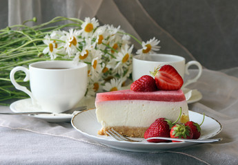 A piece of  cake, white cup of tea and bunch of daisies..