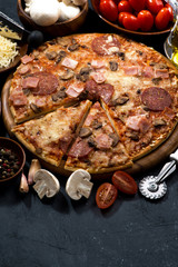 pizza with salami and ingredients on a dark background, vertical