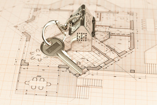 key with keychain in the form of a silver-colored house on a background of architectural drawing