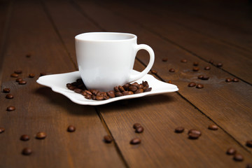 Aromatic coffee in white cup with saucer and scattered beans