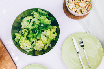 Fresh mixed green salad in bowl and zucchini on wooden table