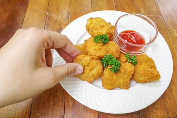 Hand picking chicken nugget in white plate on wood background