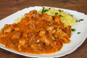 meat in sauce with mashed potatoes in a plate on wooden table