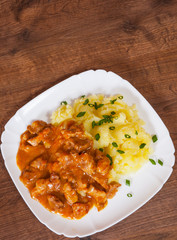 meat in sauce with mashed potatoes in a plate on wooden table
