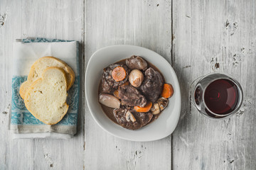Beef bourguignon in a white ceramic dish with slices of baguette