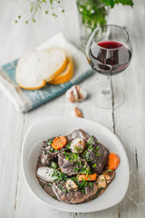 Beef bourguignon in a white ceramic plate with a glass of wine