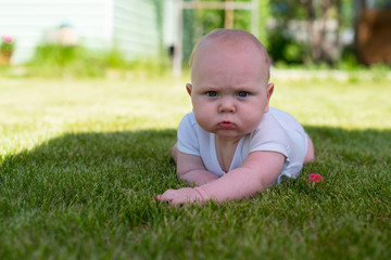 child is lying on the grass in the garden and frowns